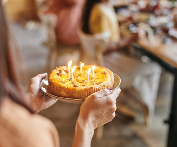 Close-up of woman carrying plate with homemade cake and candles to the table at the birthday party